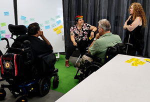 Group of people with disability sitting around a whiteboard with colour photos. 